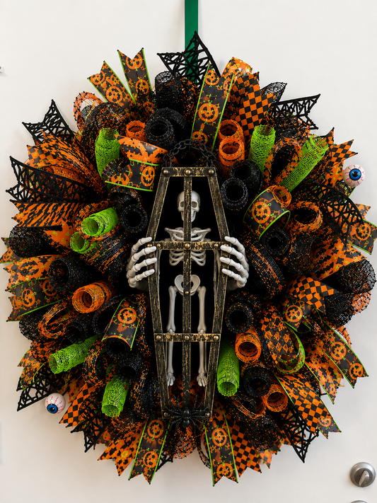 Handmade Skeleton Coffin Halloween Wreath featuring a skeleton trapped inside a distressed coffin with skeleton hands, premium black, orange, and lime green deco mesh, and designer ribbons for haunted house front door decor.